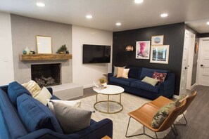 A modern living room with a fireplace, a blue sofa, a coffee table, and a TV mounted on the wall. - The Frontier Getaway (Nashville)