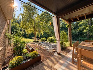 An outdoor patio area with a wooden table and chairs, surrounded by a garden with various plants and a stone pathway. - The Frontier Getaway (Nashville)