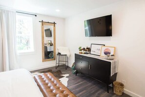 A modern bedroom with a large bed, a bench, a dresser, a TV, and a window with curtains. - The Frontier Getaway (Nashville)