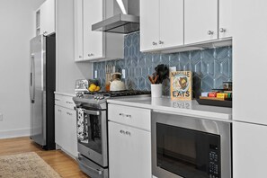 Uma cozinha moderna com eletrodomésticos de aço inoxidável, armários brancos e uma parede de backsplash revestida em azulejos azuis.
