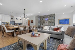 Uma sala de estar moderna com um sofá cinzento, uma mesa de centro e um espaço de jantar com mesa e cadeiras de madeira.