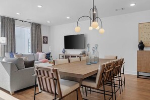 A modern living room with a grey sofa, wooden dining table, and chairs. A flat-screen TV is mounted on the wall, and there are decorative vases on the table. - Sleeps 20: Views, HotTub, FirePit, Grill, Parking (Nashville)