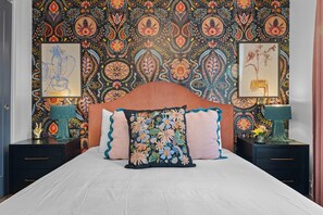 A bedroom with a patterned wallpaper, a headboard, two bedside tables with lamps, and a bed with floral pillows. - Rooftop Hot Tub Views  Parking Mins to Bway (Nashville)