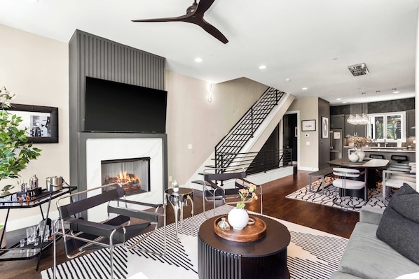 Un salon moderne avec une cheminée, un tapis rayé noir et blanc et une table basse ronde surmontée d’un vase.
