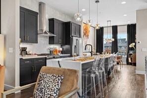A modern kitchen with dark cabinetry, a stainless steel range hood, and a central island with bar stools. - The Groovy Songwriter | Gated | Sauna + Peloton (Nashville)