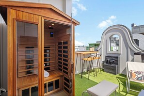 Een houten constructie met een glazen omheining, een tafeltje met stoelen en een waterpartij.