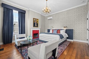 A hotel room with a bed, a chair, a table, a fireplace, and a chandelier. - The Monroe Suite | Germantown Inn | Breakfast (Nashville)