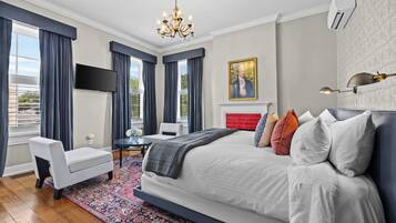 A bedroom with a large bed, a TV, a fireplace, and a chandelier.