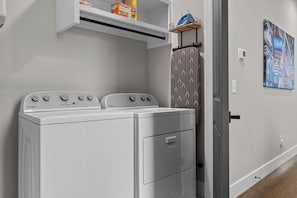A laundry area with two front-loading Whirlpool washers, a shelf with laundry detergent, and a door leading to another room. - Broadway Honky Tonk Haven w/ Karaoke Stage! (Nashville)