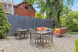 An outdoor patio with a brick floor, a wooden table with chairs, a sofa with cushions, and a wooden fence. - The Parks Suite | Germantown Inn | Breakfast (Nashville)