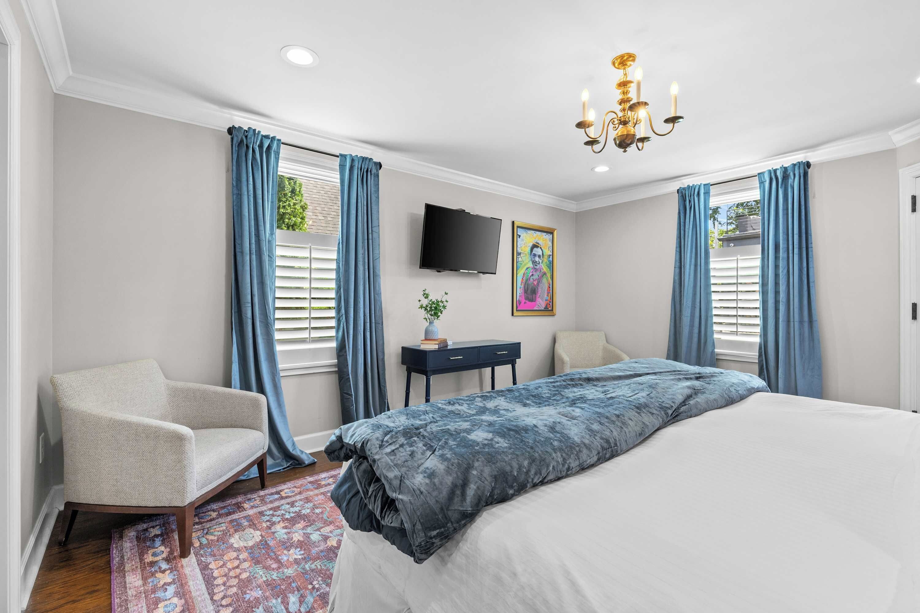 A bedroom with a large bed, a desk, a chair, a television, and a chandelier.