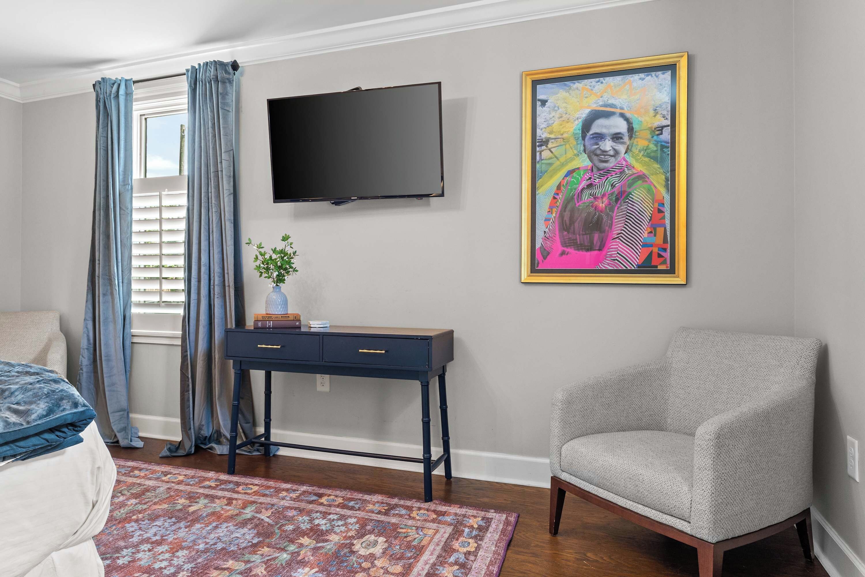 Een slaapkamer met een bed, bureau, stoel, televisie en een schilderij aan de muur.