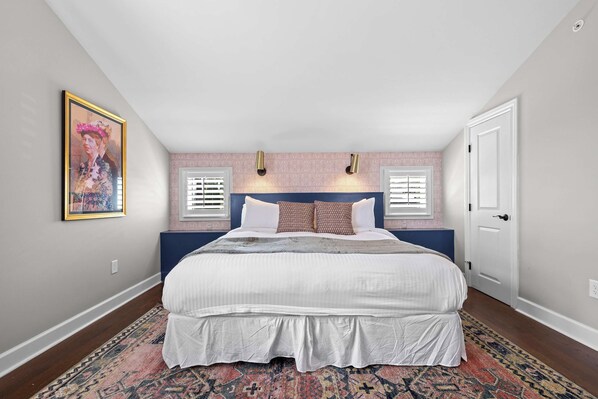 A bedroom with a large bed, two wall-mounted lights, a door, and a patterned rug. - The Roosevelt Suite | Germantown Inn | Breakfast (Nashville)