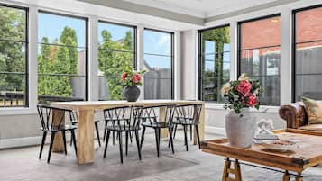A spacious room with large windows, a wooden dining table, black chairs, and a sofa with a decorative pillow.