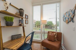 A room with a wooden desk, a brown sofa, and a window with blinds. - East Nash Stay Near Hotspots (Nashville)