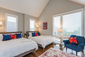 A hotel room with two beds, a blue armchair, and a small table with a lamp. - East Nash Stay Near Hotspots (Nashville)