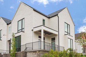 Une maison moderne à deux étages, dotée d’un balcon, de grandes fenêtres et de fondations en pierre.