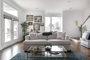 A living room with a beige sofa, a glass coffee table with a bonsai, and a staircase to the right. - East Nash Stay Near Hotspots (Nashville)
