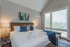 Habitación de hotel con una cama grande, dos lámparas de noche, vistas a través de las persianas y un cuadro en la pared.