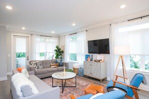 A modern living room with a sofa, a coffee table, a TV, and a window with curtains. - Chic 3BR + Free 2-Car Garage | Near Downtown (Nashville)