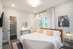 Une chambre à coucher avec un grand lit, une table de chevet avec une lampe, un miroir et un tableau encadré accroché au mur.