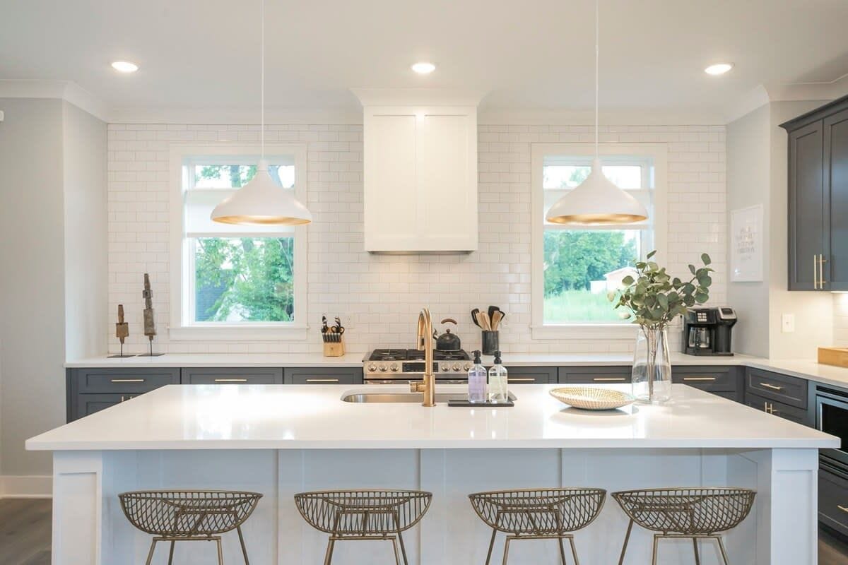 A modern kitchen with white cabinetry, a large island with bar stools, pendant lighting, and a view of greenery outside.