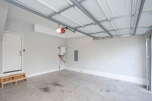 A clean, empty garage with a white door, a wooden step, and a ceiling with visible ductwork. - Chic 3BR + Free 2-Car Garage | Near Downtown (Nashville)