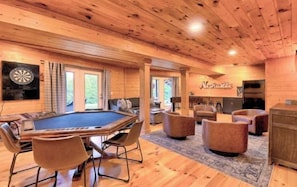 Un intérieur en bois comprenant une table de billard, un coin salon et un jeu de fléchettes.