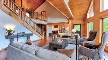 A spacious living area with a staircase, wooden flooring, and a mix of seating arrangements including a sofa and armchairs.