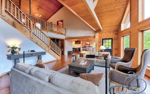 A spacious living area with a staircase, wooden flooring, and a mix of seating arrangements including a sofa and armchairs. - 5 BR Luxury Cabin | Pool, Hot Tub & Game Room (Franklin)