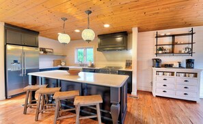 Une cuisine moderne dotée d’un îlot central, de tabourets de bar, d’appareils électroménagers en acier inoxydable et d’un revêtement de sol en bois.