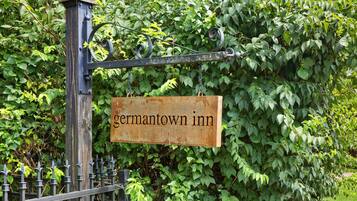 Een bord met de naam Germantown Inn, bevestigd aan een metalen paal met een ketting, omgeven door dichte begroeiing.