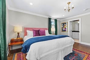 A bedroom with a bed, a nightstand, a lamp, a painting, and a door leading to a bathroom. - The Adams Suite | Germantown Inn | Breakfast (Nashville)