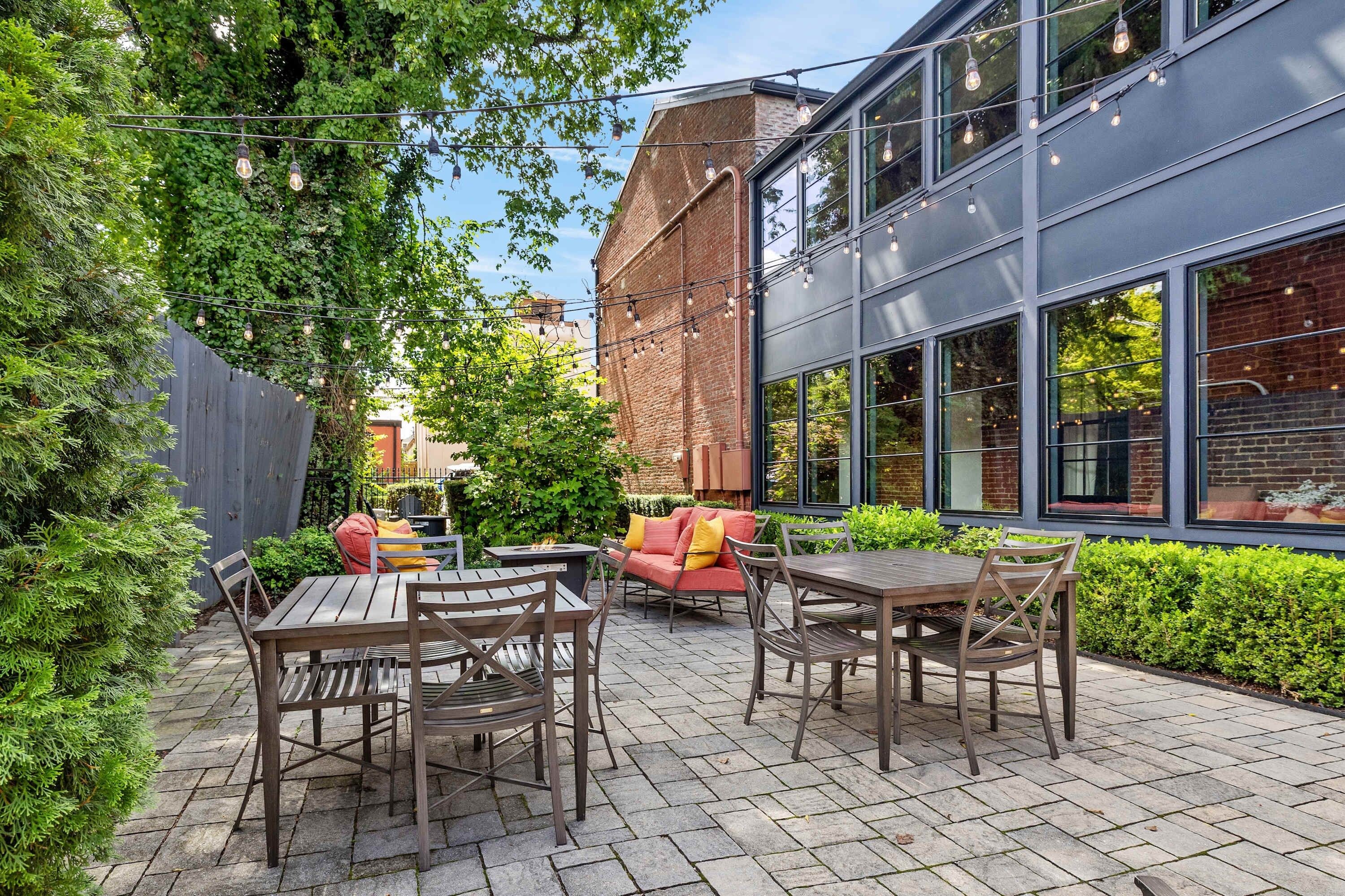 An outdoor patio with wooden tables and chairs, a red sofa, and a fire pit.