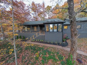 Une maison moderne dotée d’un porche abrité, d’un escalier menant à l’entrée et d’un jardin bien entretenu parsemé de feuilles d’automne.
