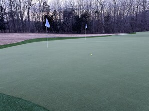 Un parcours de golf avec un green d’entraînement, des drapeaux et un paysage boisé en arrière-plan.