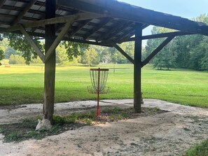A disc golf basket under a wooden pavilion with a grassy field in the background. - 65Acres HotTub, Sauna, Cold Plunge, Fishing + Golf (Joelton)