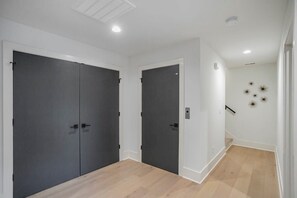 A hallway with two dark-colored doors, a light-colored wall with a decorative star pattern, and a wooden floor. - 30 Night + Luxurious Green Hills Gem! (Nashville)