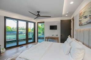 A bedroom with a large bed, a ceiling fan, a TV, and a view of a tennis court through the sliding glass doors. - 30 Night + Luxurious Green Hills Gem! (Nashville)
