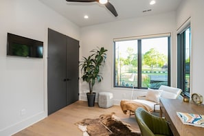 A modern living room with a large window, a ceiling fan, a flat-screen TV, a potted plant, a leather sofa, and a wooden dining table. - 30 Night + Luxurious Green Hills Gem! (Nashville)