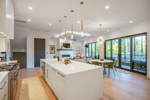 A modern kitchen with a central island, pendant lighting, and a dining area with a view. - 30 Night + Luxurious Green Hills Gem! (Nashville)