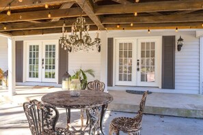 Eine Terrasse im Freien mit einem runden Tisch, Stühlen, einer Kandelaber und einem Haus mit Fensterläden.