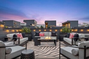 Eine Dachterrasse mit Außenbereich, Sitzgelegenheiten, einem Feuerkorb und Lichterketten.