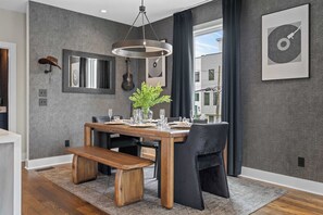 Un coin repas avec une table en bois, des chaises noires, un luminaire suspendu et une guitare accrochée au mur.