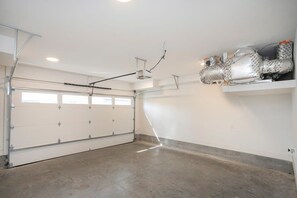 Eine geräumige Garage mit Betonboden, einer weißen Garagentür und einer Decke mit freiliegenden Balken und Beleuchtung.