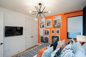 Ein modernes Wohnzimmer mit Fernseher, einer Deckenleuchte und einer Wand mit gerahmten Fotografien.