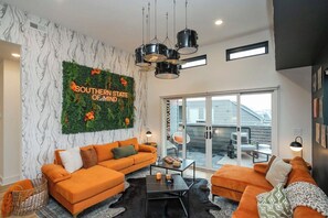 Un soggiorno moderno con due divani arancioni, un tavolino da caffè nero e un elemento decorativo verde al muro.