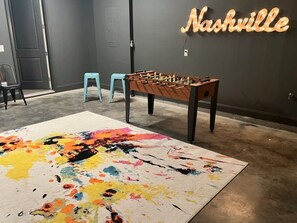 Una habitación con una mesa de futbolín, un tapete abstracto y colorido, y un letrero de neón que dice "Nashville".