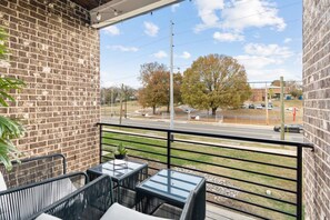 Ein Balkon mit Sitzgelegenheit, einer Backsteinmauer und Blick auf eine Straße und Bäume.