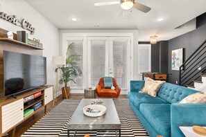 Ein modernes Wohnzimmer mit einem großen Flachbildfernseher, einem blauen Sofa, einem Couchtisch und einer Treppe.